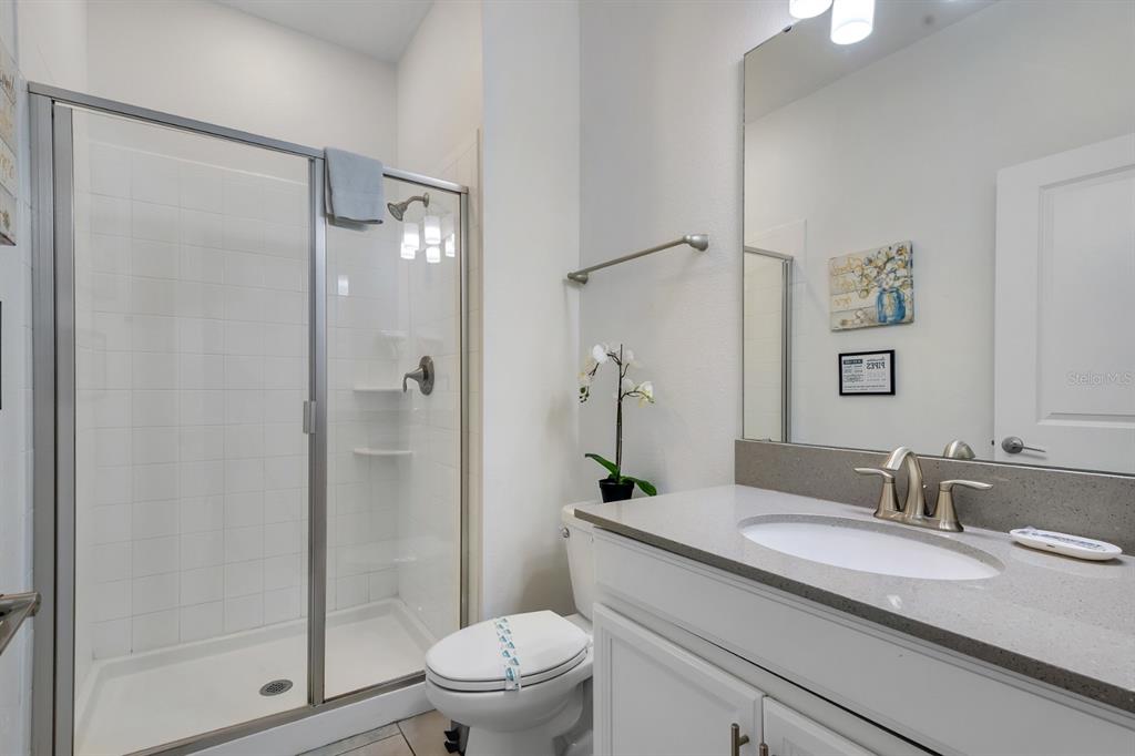 A bathroom features a glass-enclosed shower, a white vanity with a gray countertop, and toilet — 680 PEBBLE BEACH DRIVE, DAVENPORT, FL