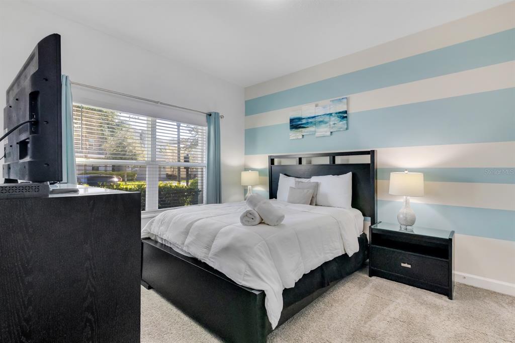 A bedroom features a bed with white bedding, a black headboard, and blue-striped walls — 680 PEBBLE BEACH DRIVE, DAVENPORT, FL