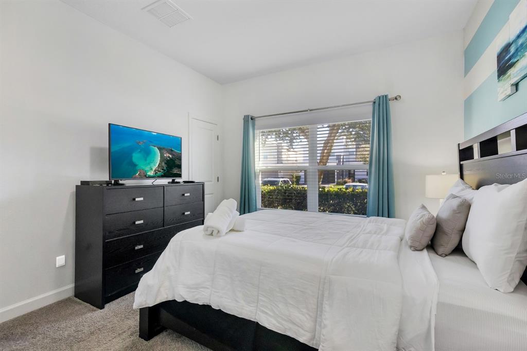 A bedroom features a bed with white bedding, a black dresser, and blue curtains — 680 PEBBLE BEACH DRIVE, DAVENPORT, FL