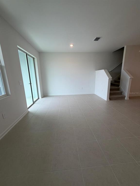 An empty room with light-colored tile flooring, a sliding glass door, and carpeted stairs — 3106 KURTZ TERRACE, DAVENPORT, FL
