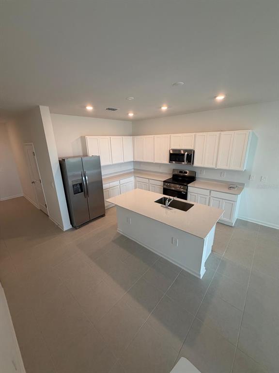 A kitchen features white cabinetry, stainless steel appliances, a center island, and light-colored tile flooring — 3106 KURTZ TERRACE, DAVENPORT, FL