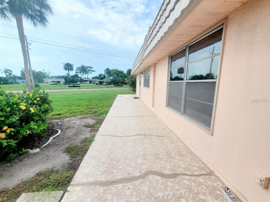 A concrete walkway runs along the side of a peach-colored house with large windows — 201 BEDFORD TRAIL UNIT 121, SUN CITY CENTER, FL