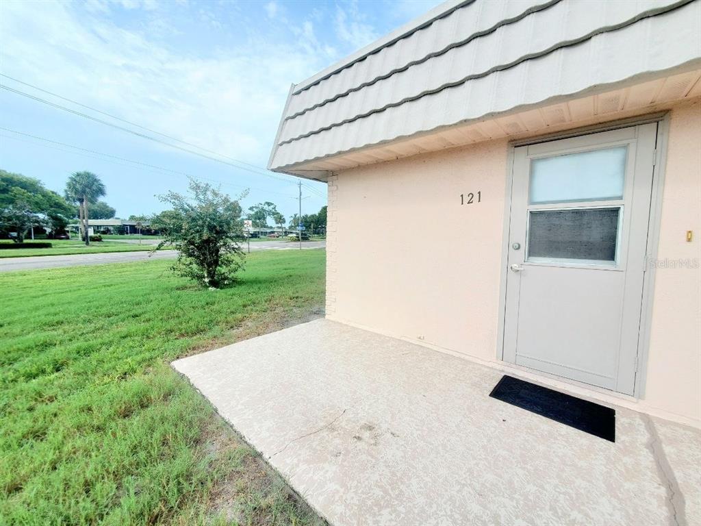 A concrete patio sits in front of a beige building entrance marked with the number 121 — 201 BEDFORD TRAIL UNIT 121, SUN CITY CENTER, FL