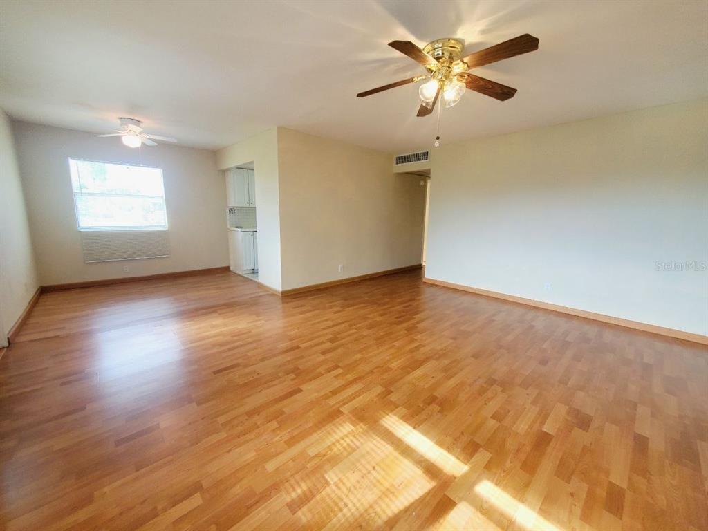 An empty living room features hardwood floors, a ceiling fan, and a window — 201 BEDFORD TRAIL UNIT 121, SUN CITY CENTER, FL