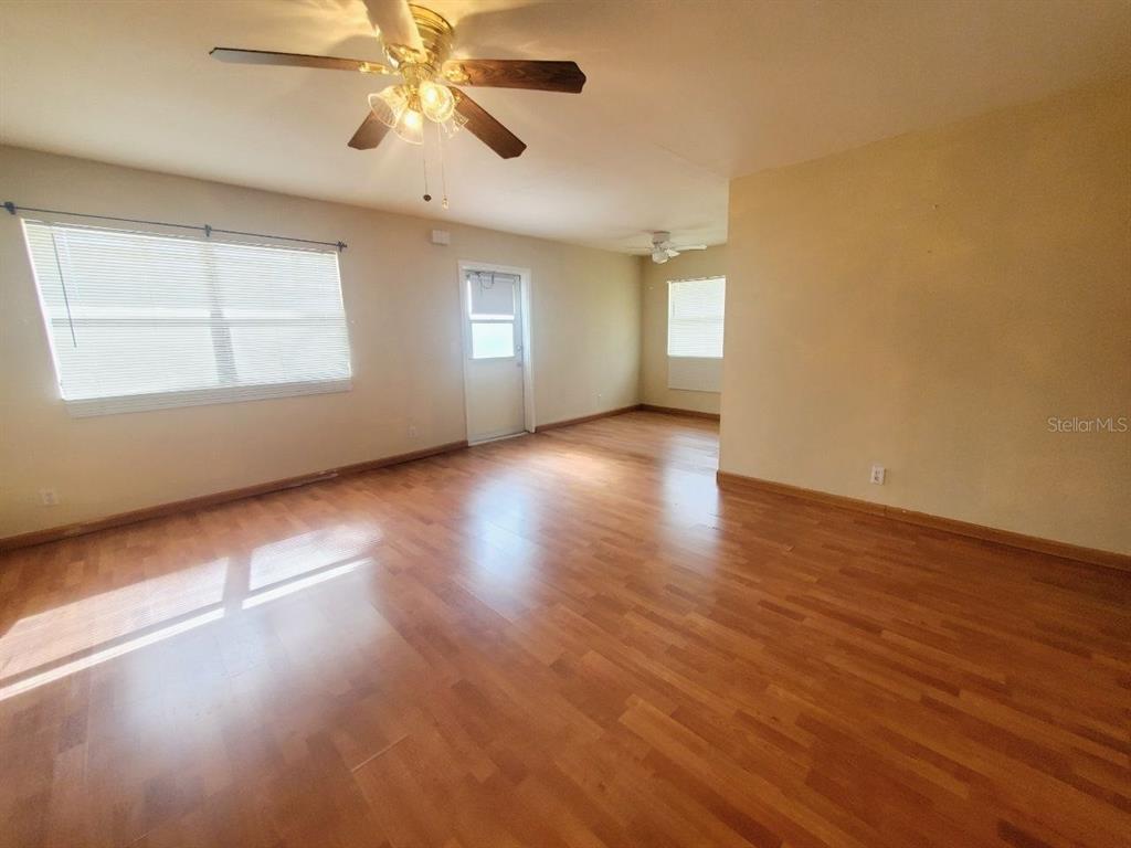 An empty room with wood-look flooring, a ceiling fan, and a white exterior door — 201 BEDFORD TRAIL UNIT 121, SUN CITY CENTER, FL