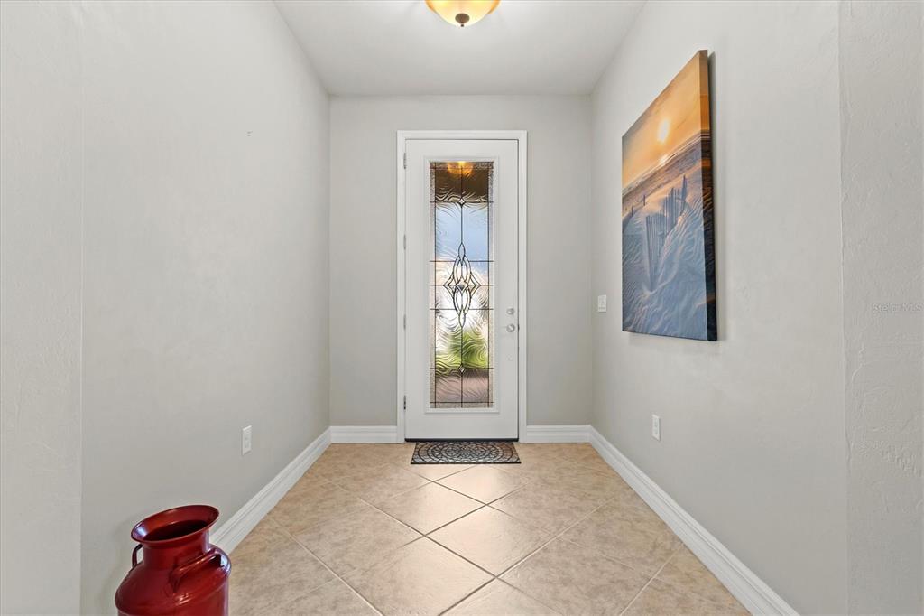 An entryway features a tiled floor, a white front door with decorative glass, and wall art — 19556 PETRINO STREET, VENICE, FL