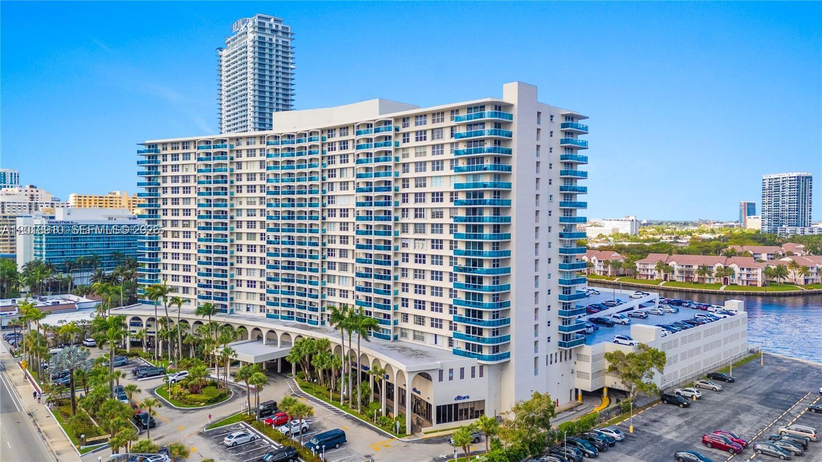 An aerial view of a large multi-story residential building with blue balconies and parking lots — 3800 S Ocean Dr # 1114, Hollywood FL 33019, HOLLYWOOD, FL