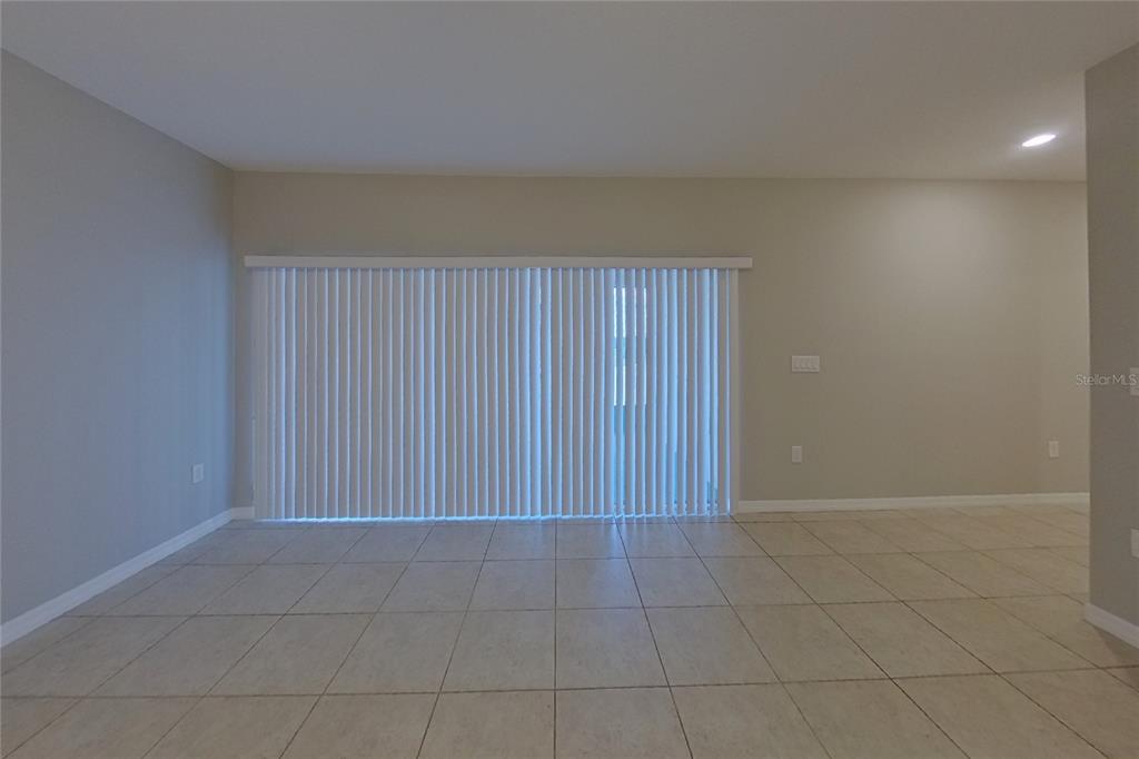 An empty room features light-colored tile flooring, beige walls, and a large sliding glass door — 417 KESTREL DRIVE, GROVELAND, FL