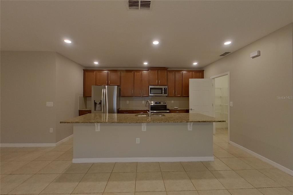 A kitchen features wood cabinets, granite countertops, a center island, and stainless steel appliances — 417 KESTREL DRIVE, GROVELAND, FL