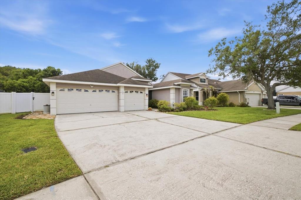 A suburban house features a three-car garage and a concrete driveway under a blue sky — 392 TAVERNIER CIRCLE, OLDSMAR, FL