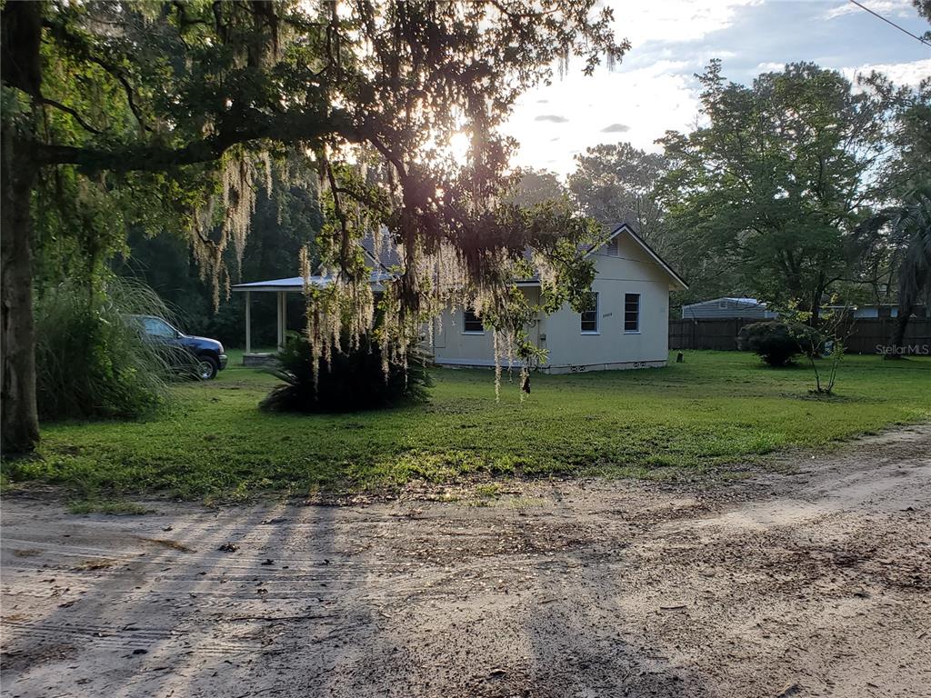 A light-colored house with a porch sits on a grassy lot under large trees — 23676 NW 194TH AVENUE, HIGH SPRINGS, FL