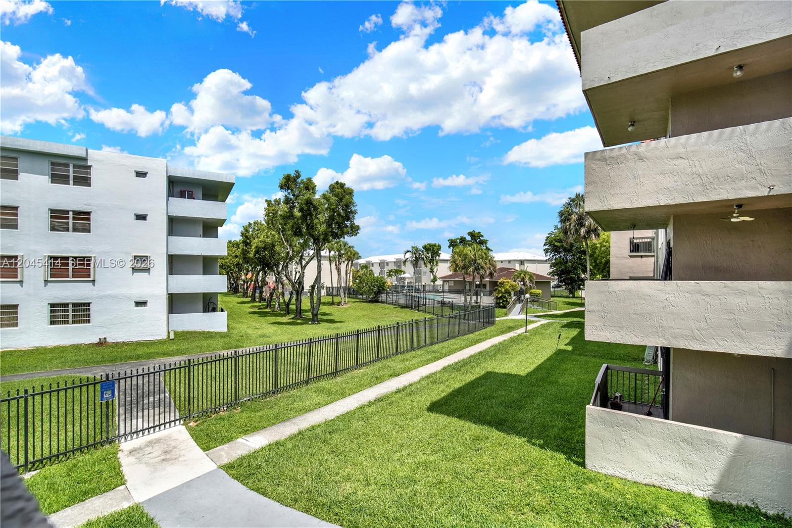 An exterior view shows apartment buildings separated by a grassy lawn and a metal fence — 1101 SW 122nd Ave # 205, Miami FL 33184, MIAMI, FL