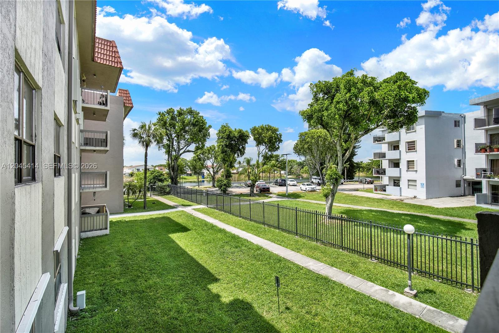 An exterior view shows a grassy courtyard with a black metal fence and apartment buildings — 1101 SW 122nd Ave # 205, Miami FL 33184, MIAMI, FL