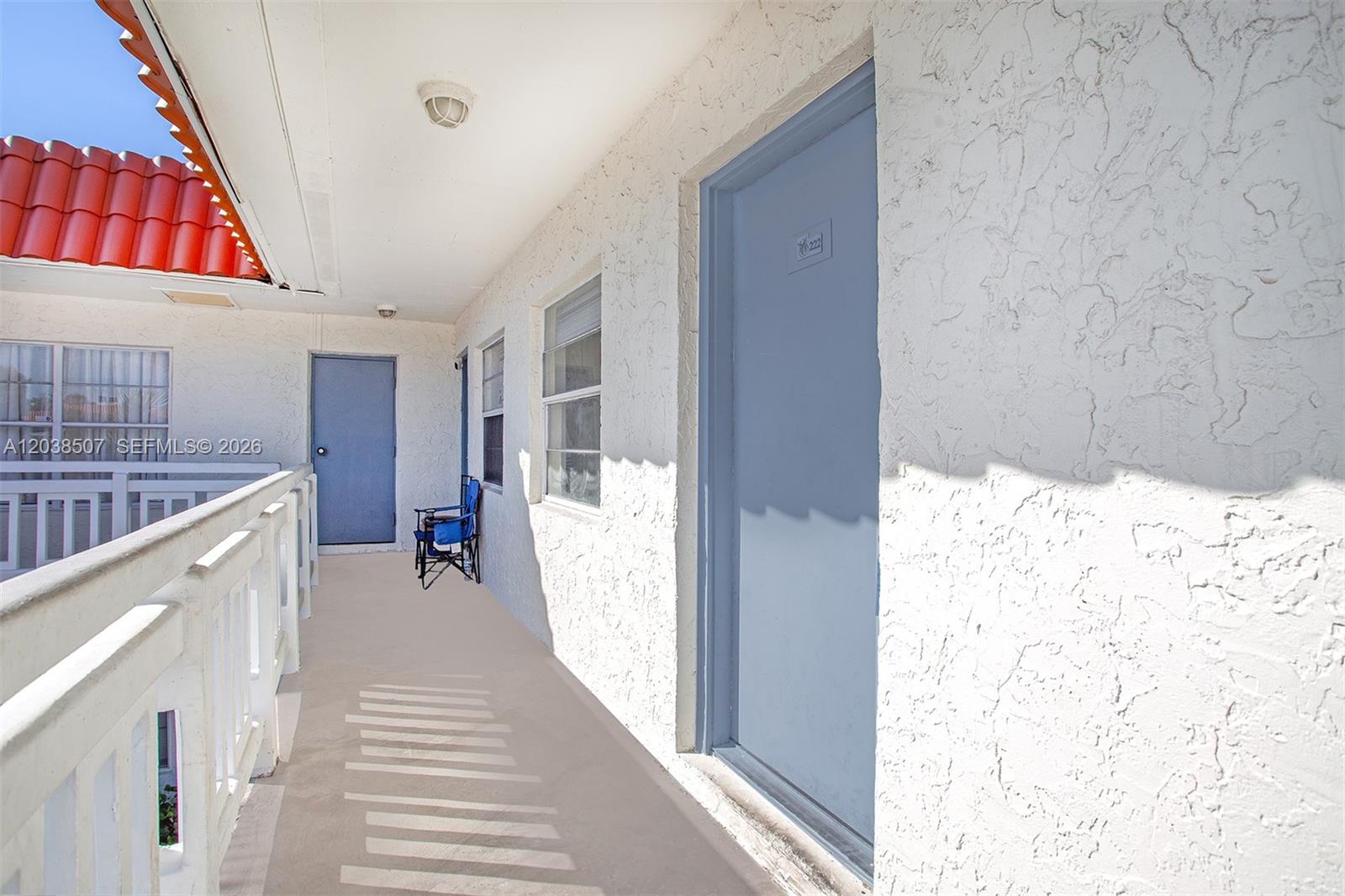 An outdoor walkway features white stucco walls, blue doors, and a red tile roof edge — 1333 S Dixie Hwy # 222, Deerfield Beach FL 33441, DEERFIELD BEACH, FL