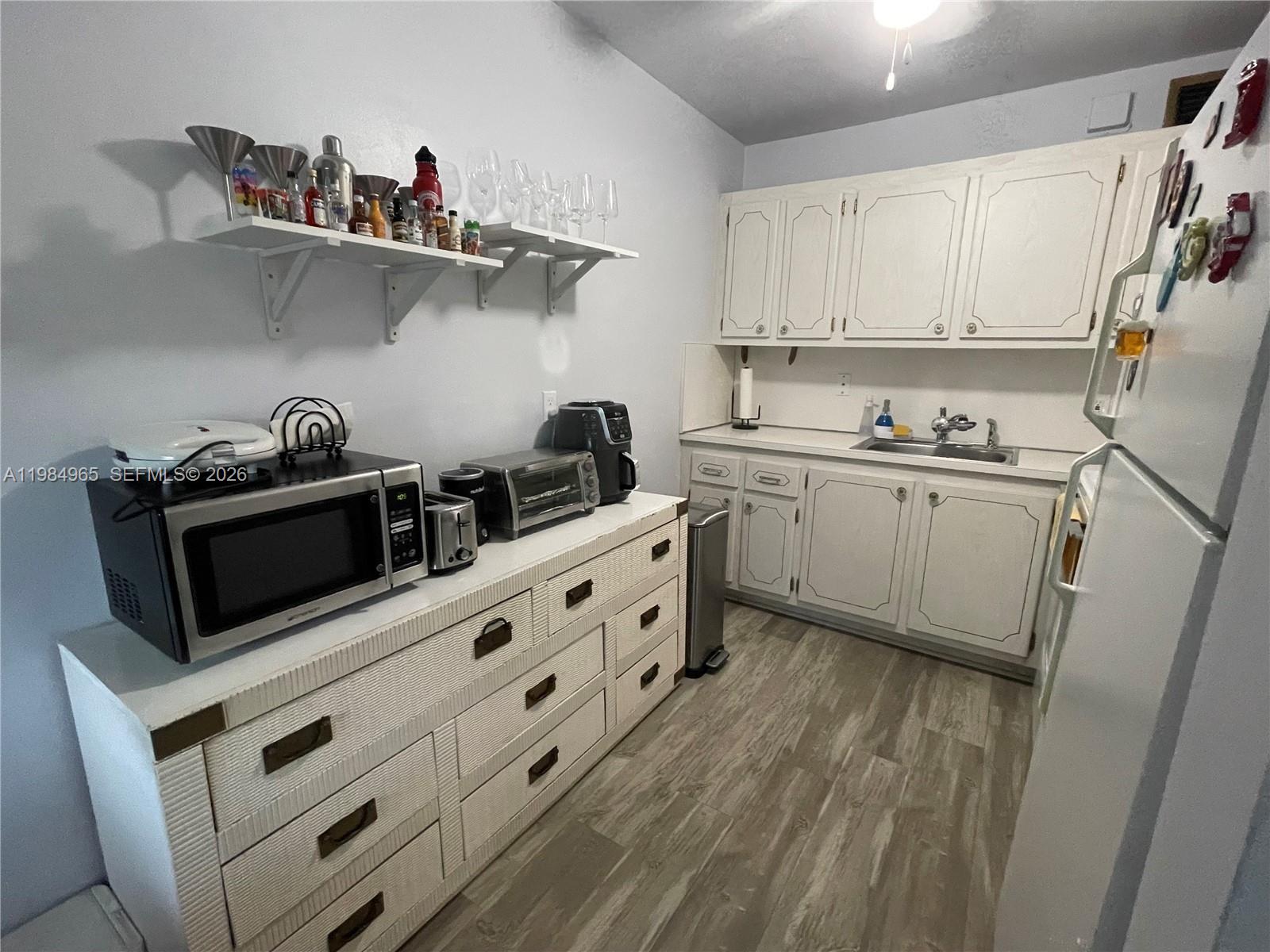 A kitchen features white cabinets, a microwave on a dresser, and open wall shelving — 279 Markham M # M, Deerfield Beach FL 33442, DEERFIELD BEACH, FL