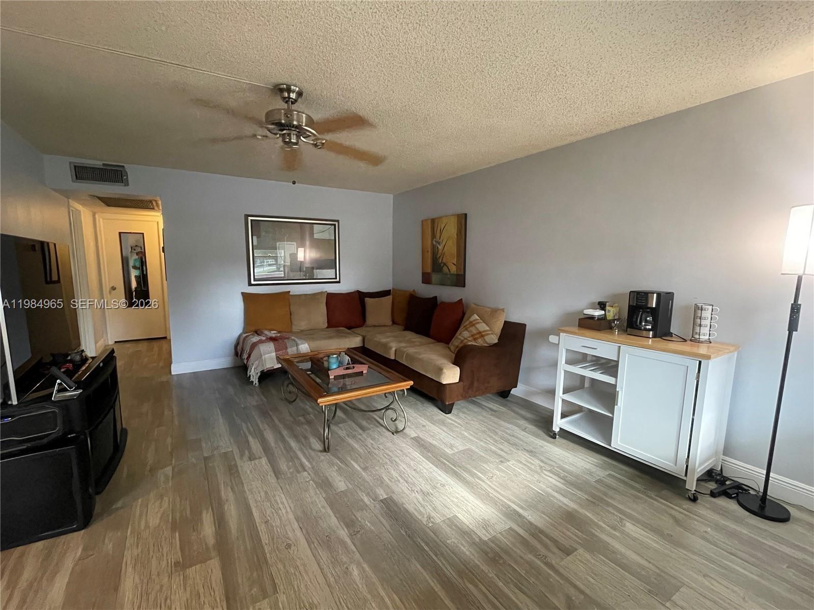 A living room features a sectional sofa, wood-look flooring, a ceiling fan, and a coffee station — 279 Markham M # M, Deerfield Beach FL 33442, DEERFIELD BEACH, FL