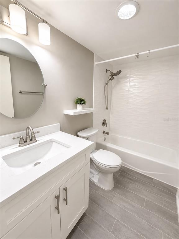 A small bathroom features a white vanity, oval mirror, wall-mounted shelf, and toilet — 1 KEY CAPRI UNIT 102W, TREASURE ISLAND, FL