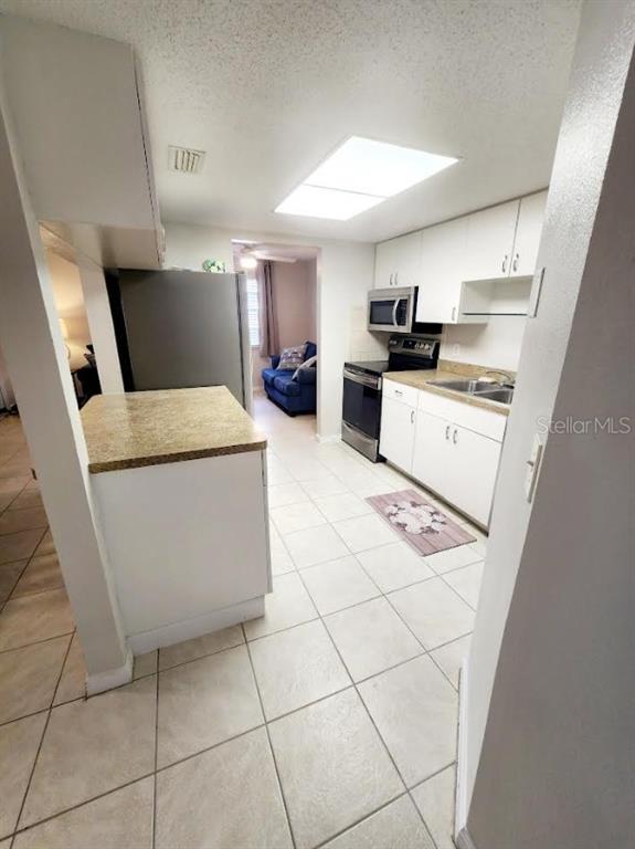 A kitchen with white cabinets, granite countertops, and tile flooring leads into a living area — 4022 BEAVER LANE UNIT 800D, PORT CHARLOTTE, FL