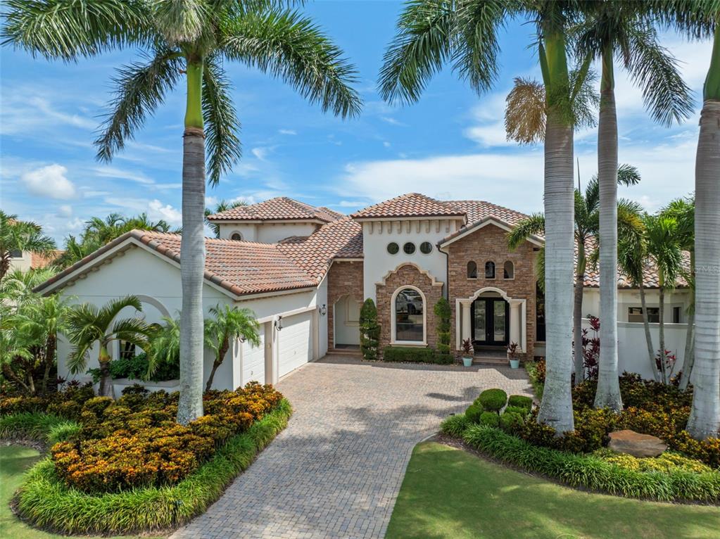A Mediterranean-style house with a stone facade, tile roof, and a paved driveway — 5405 TYBEE ISLAND DRIVE, APOLLO BEACH, FL