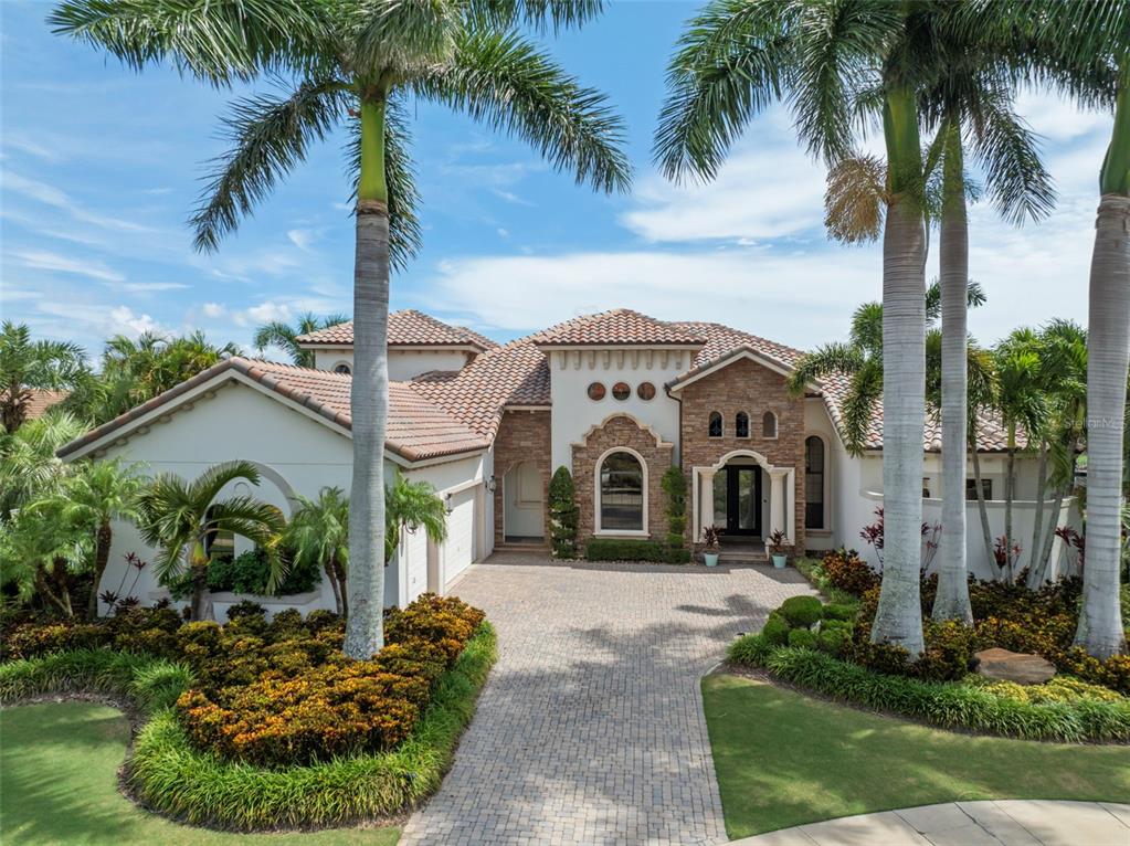 A Mediterranean-style house with a stone facade, tile roof, and a paved driveway — 5405 TYBEE ISLAND DRIVE, APOLLO BEACH, FL