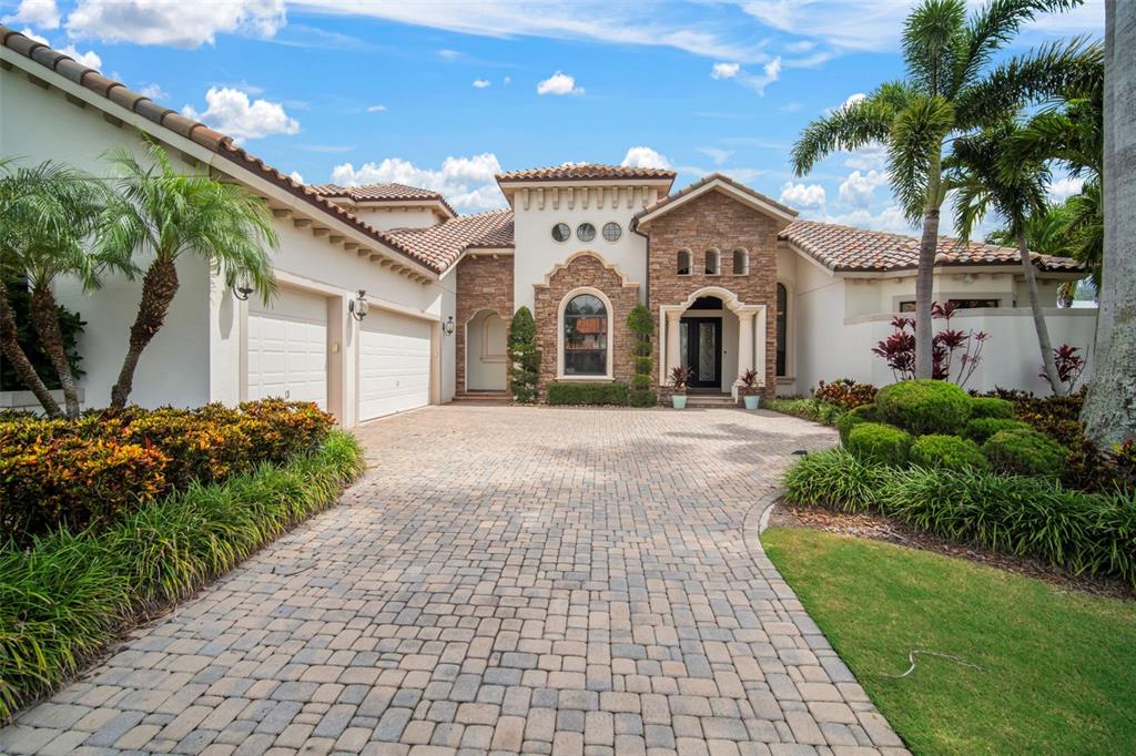 A Mediterranean-style house features a stone facade, a tiled roof, and a paved driveway — 5405 TYBEE ISLAND DRIVE, APOLLO BEACH, FL