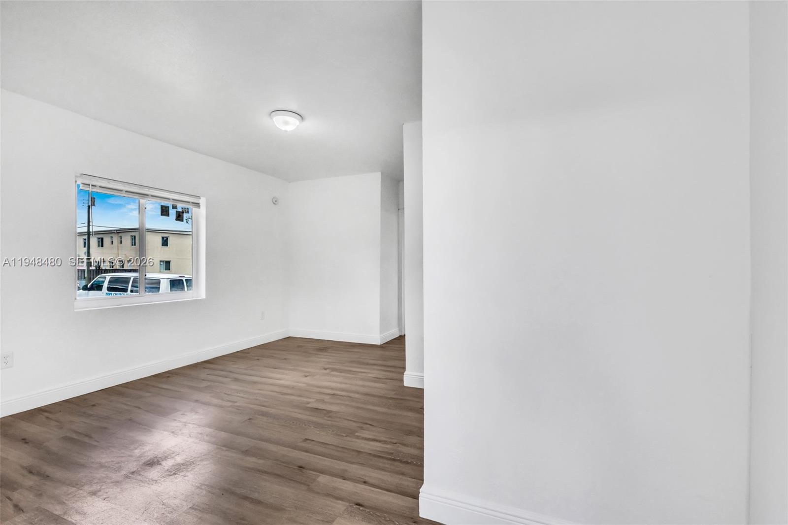 An empty room features white walls, wood-look flooring, and a window overlooking a parking lot — 8329 NW 5th Ave # 1, Miami FL 33150, MIAMI, FL