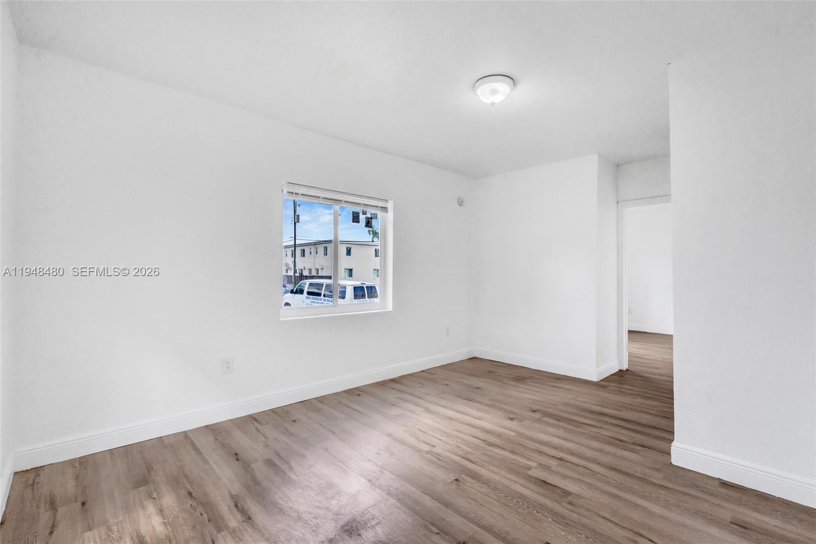An empty room features white walls, light wood-look flooring, a ceiling light, and a window — 8329 NW 5th Ave # 1, Miami FL 33150, MIAMI, FL