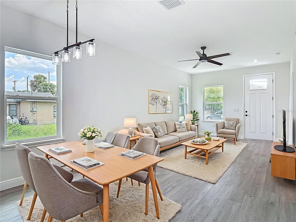 A bright open-concept living and dining area features light wood furniture, gray flooring, and rugs — 2445 DOLARWAY STREET, SANFORD, FL