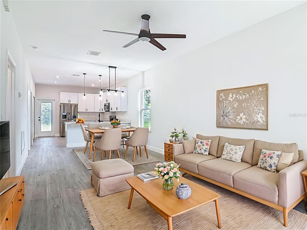 An open-concept living and dining area features light wood flooring, a neutral sofa, and kitchen — 2445 DOLARWAY STREET, SANFORD, FL