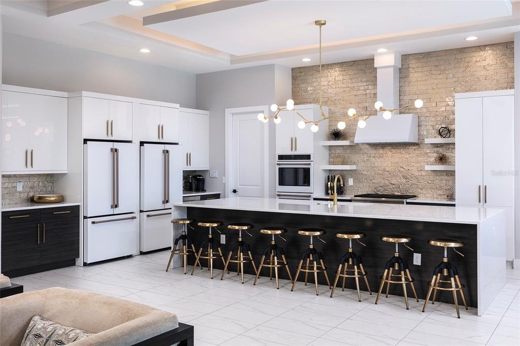 A modern kitchen features white cabinetry, a large dark island with bar stools, and stone walls — 1514 COROLLA COURT, REUNION, FL