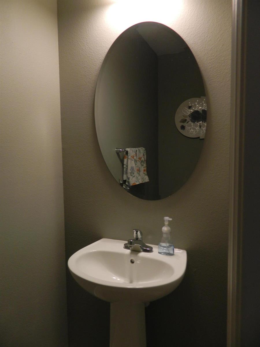 A pedestal sink with a chrome faucet sits below an oval mirror in a bathroom — 3345 Liberty Square Way # 101, Fort Pierce FL 34982, FORT PIERCE, FL