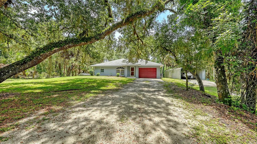 A single-story house with a red garage door sits behind a dirt driveway and trees — 4498 HIDDEN RIVER ROAD, SARASOTA, FL