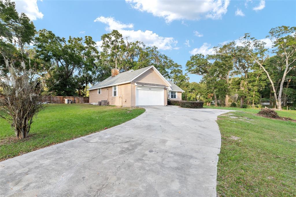 A tan house with a white garage door and a concrete driveway surrounded by trees — 9161 SW 34TH PLACE, OCALA, FL