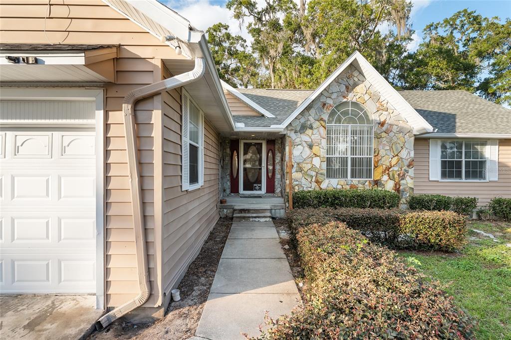 A house exterior featuring tan siding, a stone facade, a garage, and a front walkway — 9161 SW 34TH PLACE, OCALA, FL