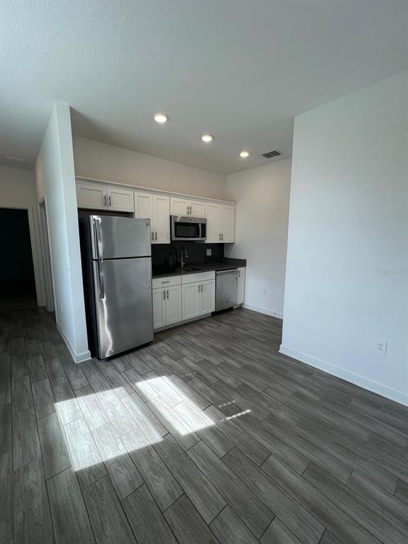 An open-concept living area features light wood-look tile flooring, a kitchen island, and sliding doors — 2817 CAMDEN WAY, DAVENPORT, FL
