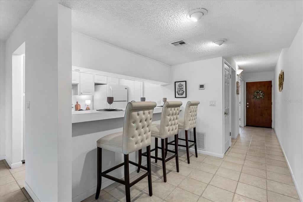 A kitchen breakfast bar with three tufted stools overlooks a tiled hallway and entryway — 510 CRANES WAY UNIT 206, ALTAMONTE SPRINGS, FL