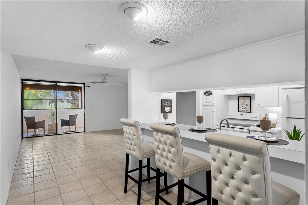 A kitchen with a breakfast bar and stools overlooks an open living area with tile floors — 510 CRANES WAY UNIT 206, ALTAMONTE SPRINGS, FL