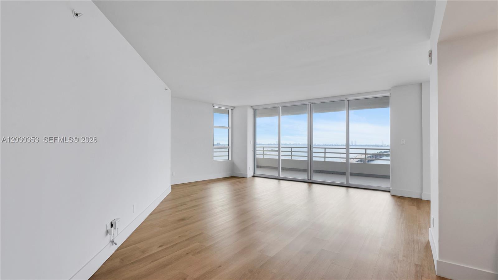 An empty room with light wood flooring, white walls, and a balcony overlooking water — 555 NE 34th St # 1601, Miami FL 33137, MIAMI, FL