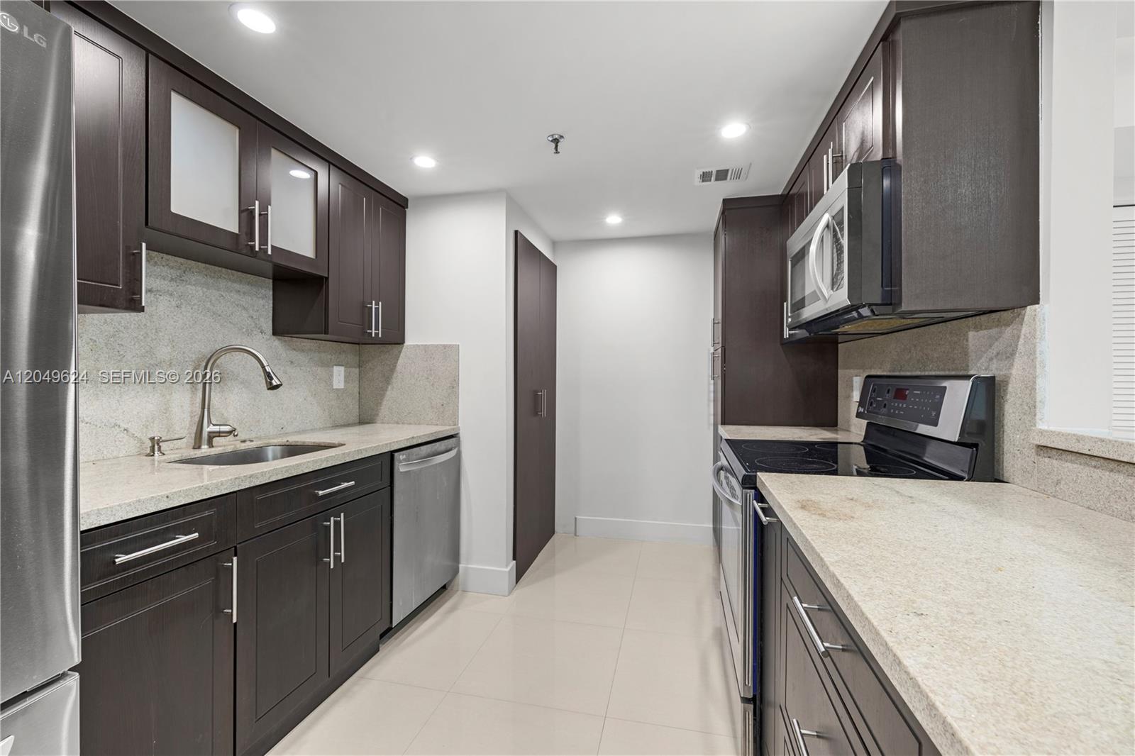 A galley kitchen features dark wood cabinets, stainless steel appliances, and light granite countertops — 2457 Collins Ave # 307, Miami Beach FL 33140, MIAMI BEACH, FL