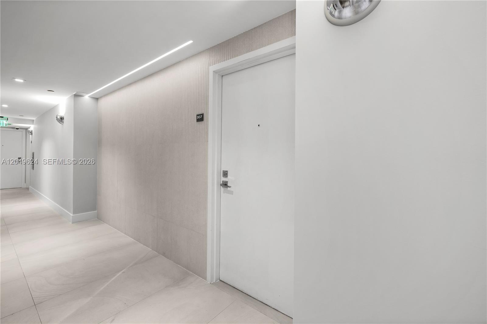 A white door with the number 307 is located in a modern, minimalist hallway — 2457 Collins Ave # 307, Miami Beach FL 33140, MIAMI BEACH, FL