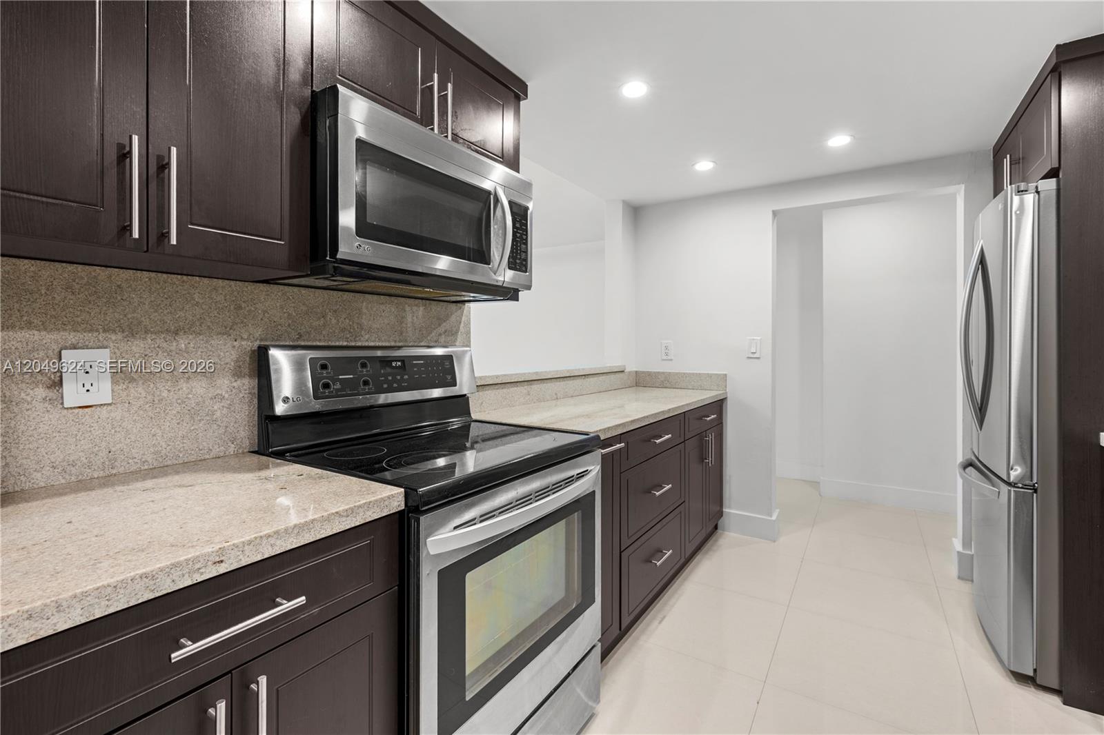 A kitchen features dark wood cabinets, stainless steel appliances, and light-colored granite countertops — 2457 Collins Ave # 307, Miami Beach FL 33140, MIAMI BEACH, FL