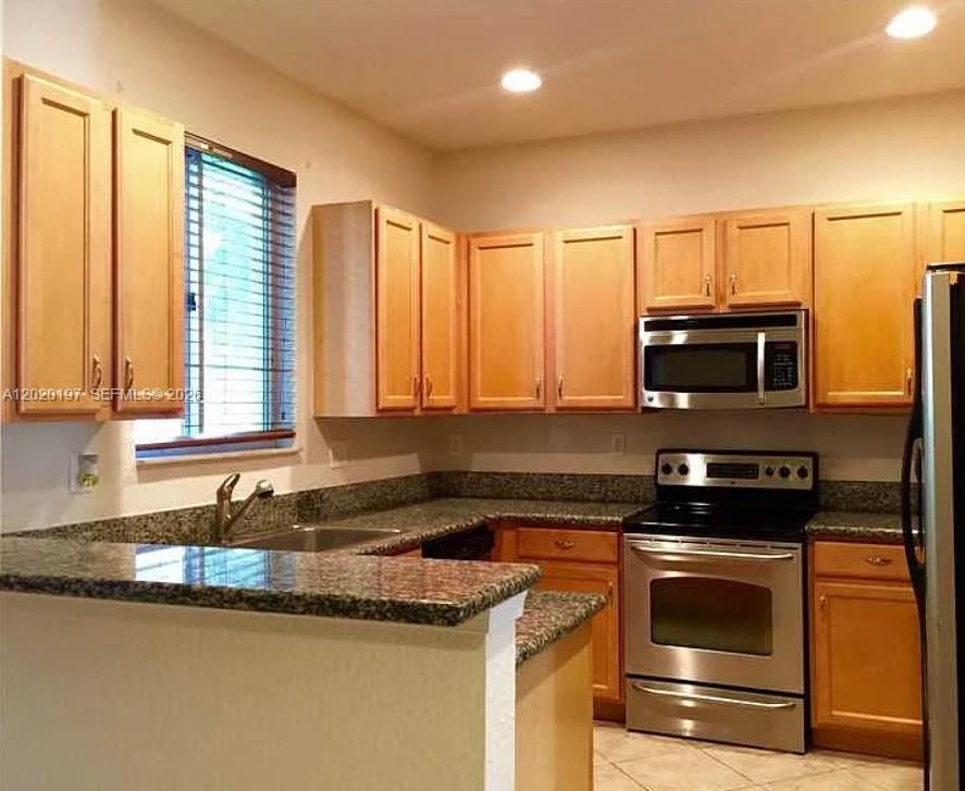 A kitchen features light wood cabinets, granite countertops, and stainless steel appliances — 21115 NW 14th Pl # 2, Miami Gardens FL 33169, MIAMI GARDENS, FL