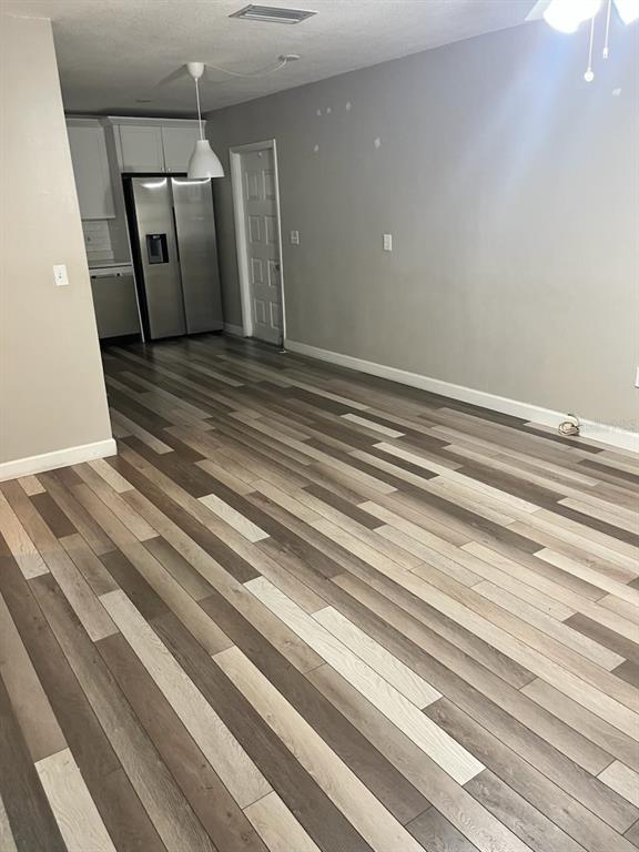 An open-concept room features multi-toned wood-look flooring, gray walls, and a stainless steel refrigerator — 3810 W CLEVELAND STREET UNIT B, TAMPA, FL