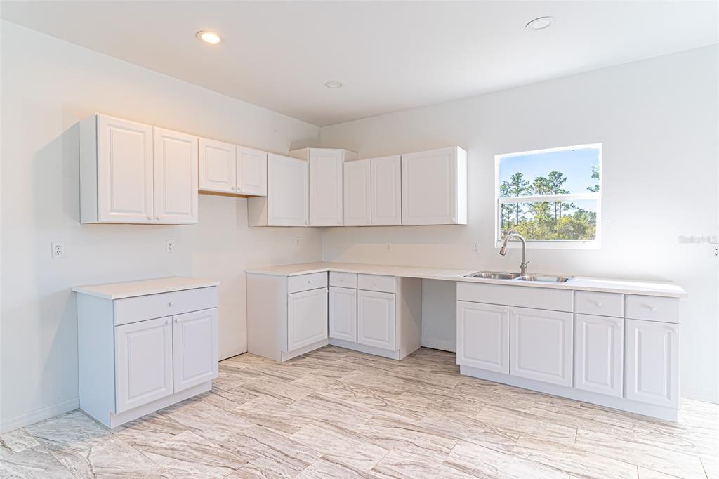 A kitchen features white cabinets, light countertops, a stainless steel sink, and wood-look tile flooring — 1403 BITTERSWEET STREET, LAKE PLACID, FL
