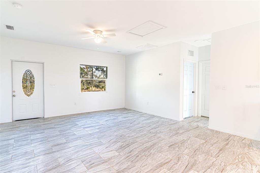 A bright, empty room features white walls, a ceiling fan, and light-colored marble-patterned tile flooring — 1403 BITTERSWEET STREET, LAKE PLACID, FL