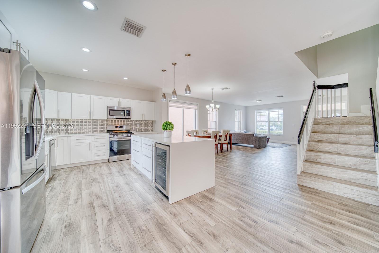 A modern open-concept kitchen with white cabinetry, a center island, and wood-look tile flooring — 15261 SW 108th Ter, Miami FL 33196, MIAMI, FL