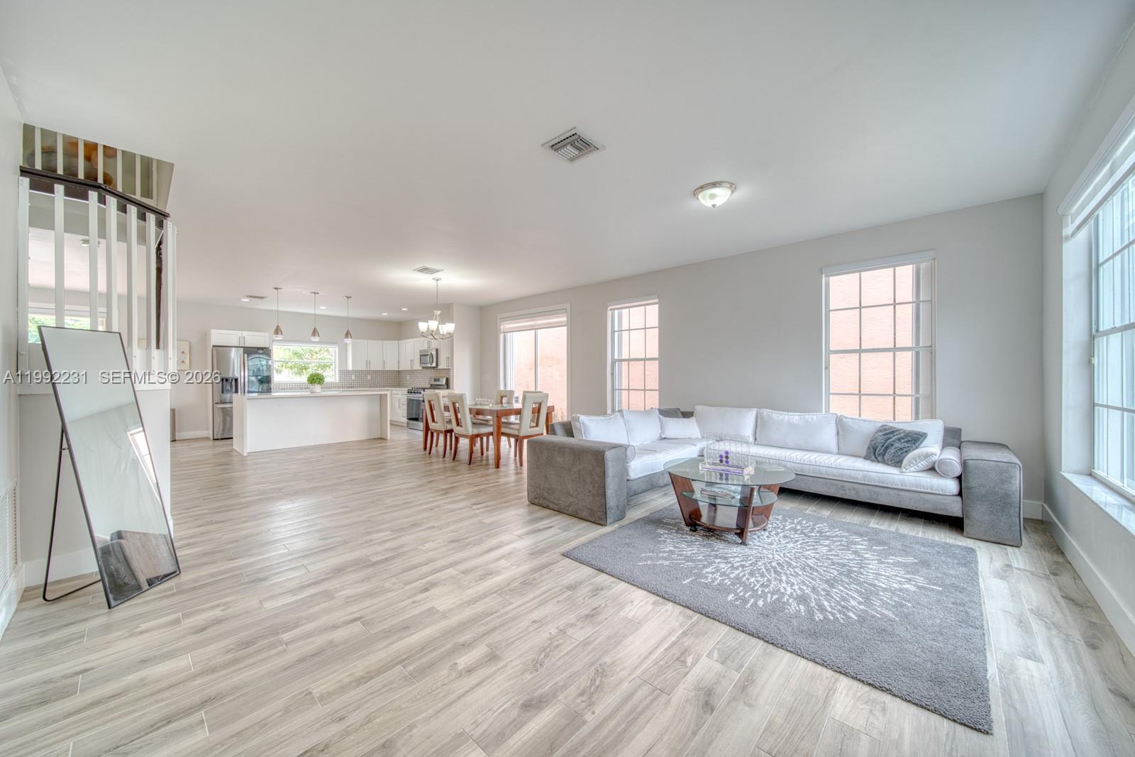 An open-concept living and dining area features light wood-look flooring, a white sectional, and kitchen — 15261 SW 108th Ter, Miami FL 33196, MIAMI, FL