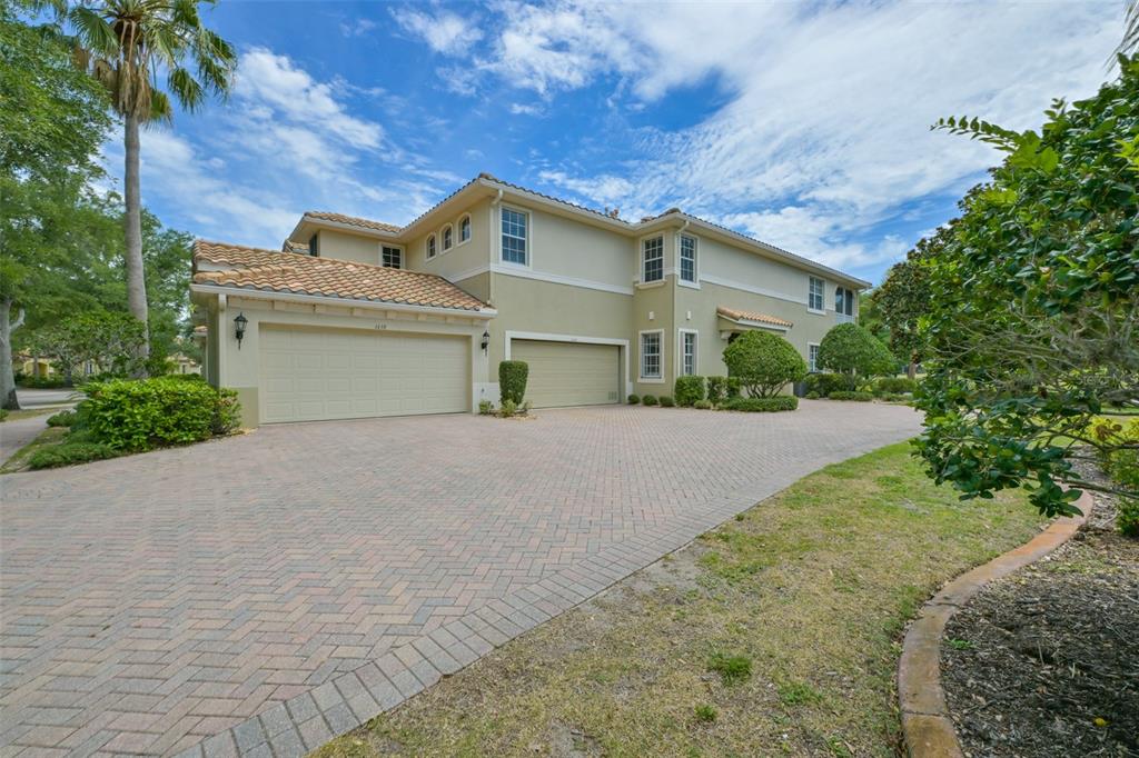 A two-story house with a beige exterior, tile roof, and a large brick-paved driveway — 1440 EMERALD DUNES DRIVE, SUN CITY CENTER, FL