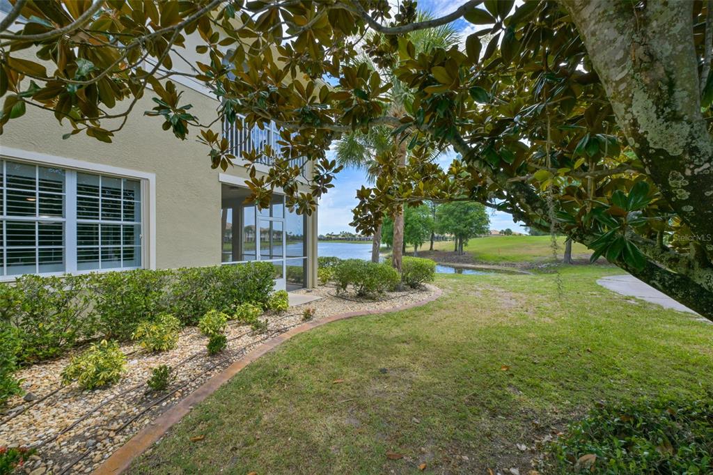 A view of a tan building exterior with a screened porch overlooking a small lake — 1440 EMERALD DUNES DRIVE, SUN CITY CENTER, FL