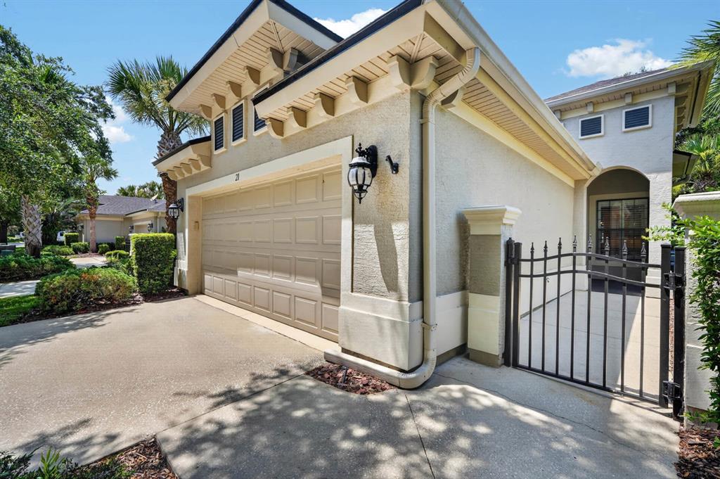 A beige stucco house exterior features a two-car garage, a black metal gate, and landscaping — 21 RIVER LANDING DRIVE, PALM COAST, FL